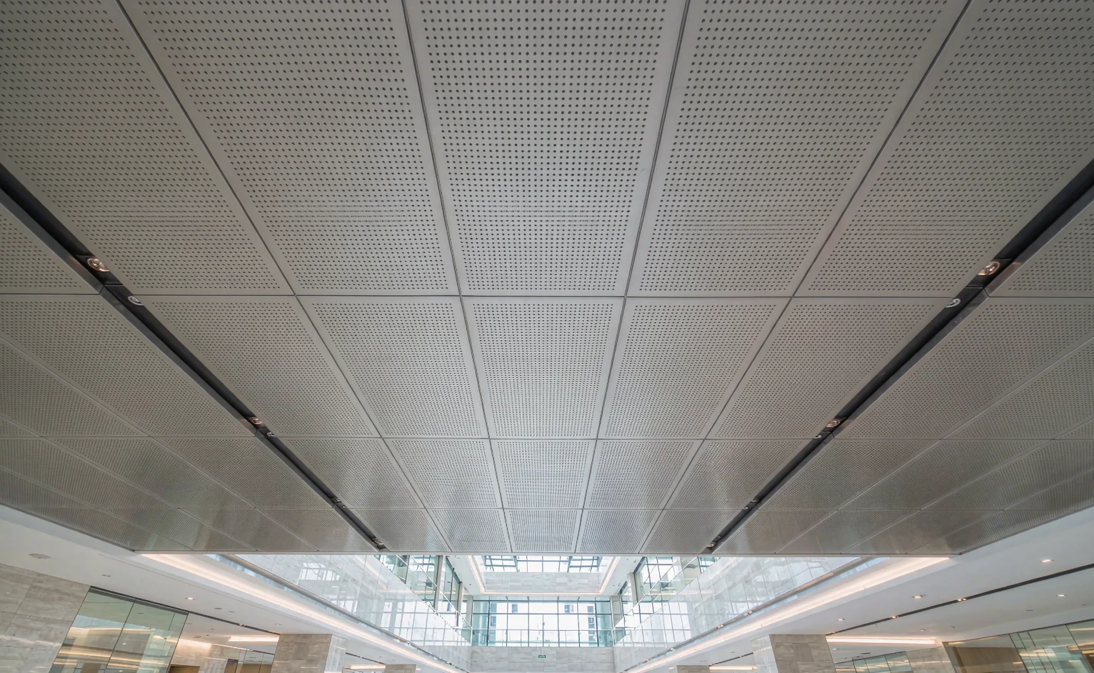 Commercial lobby ceiling of perforated aluminium clip-in panels 600 by 600 mm on an exposed suspension grid