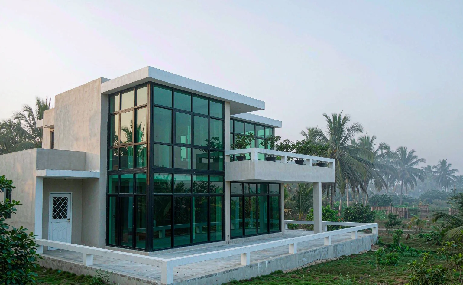 Modern two-storey villa on the West African Atlantic coast with large aluminium framed glazing and palm trees behind