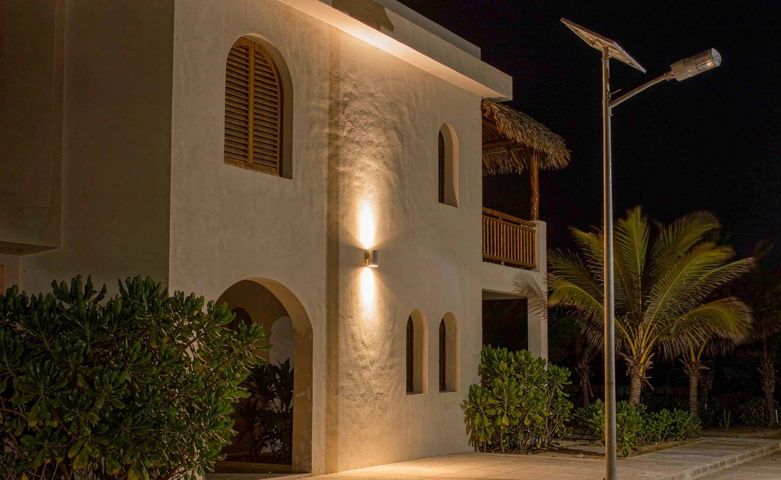 Coastal villa facade at night lit by IP65 exterior wall lights with a solar LED street light pole in the foreground