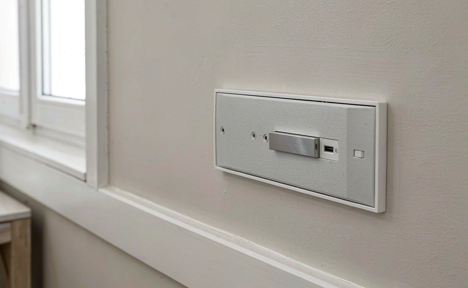 Close-up of a white 86 x 86 mm switch and socket plate with USB outlet on a plaster wall in a hot climate interior