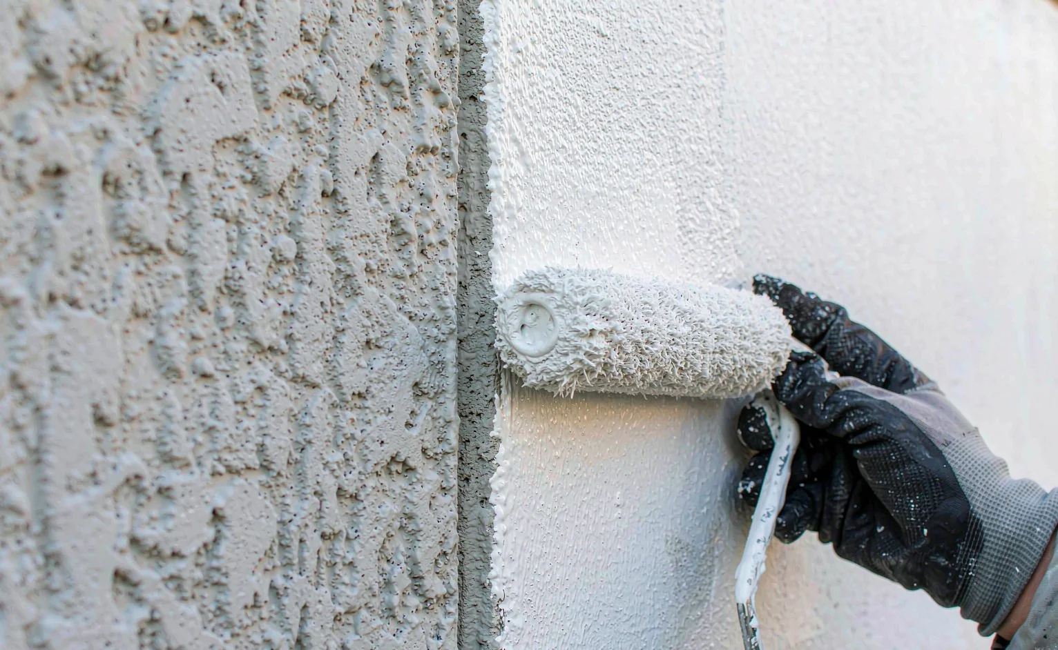 Worker with roller applying white elastomeric anti-crack exterior coating to a concrete wall on site