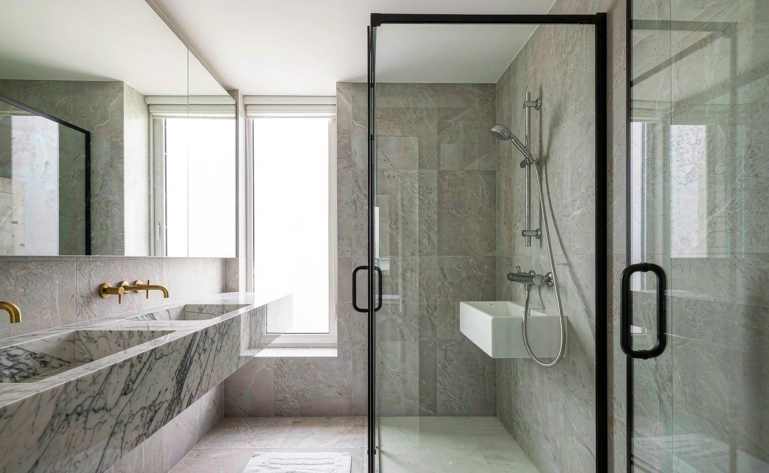 Hotel bathroom with wall-hung sanitary ware, large-format porcelain tiles, brass fittings and glass shower partition