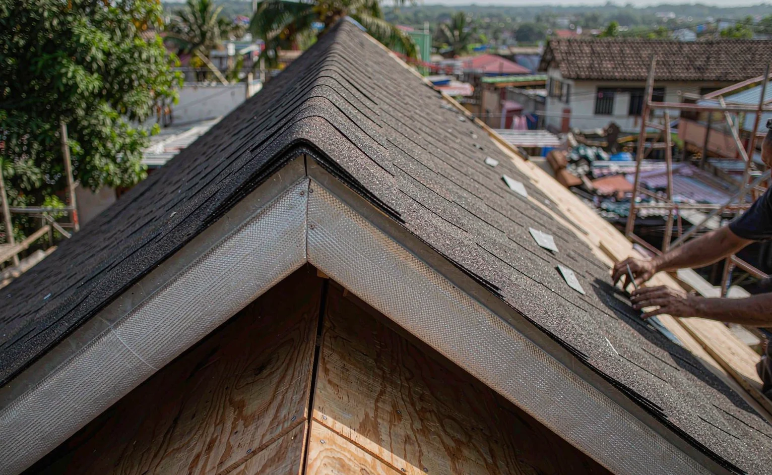 Asphalt shingle roof being laid over underlayment and plywood decking on a tropical building site