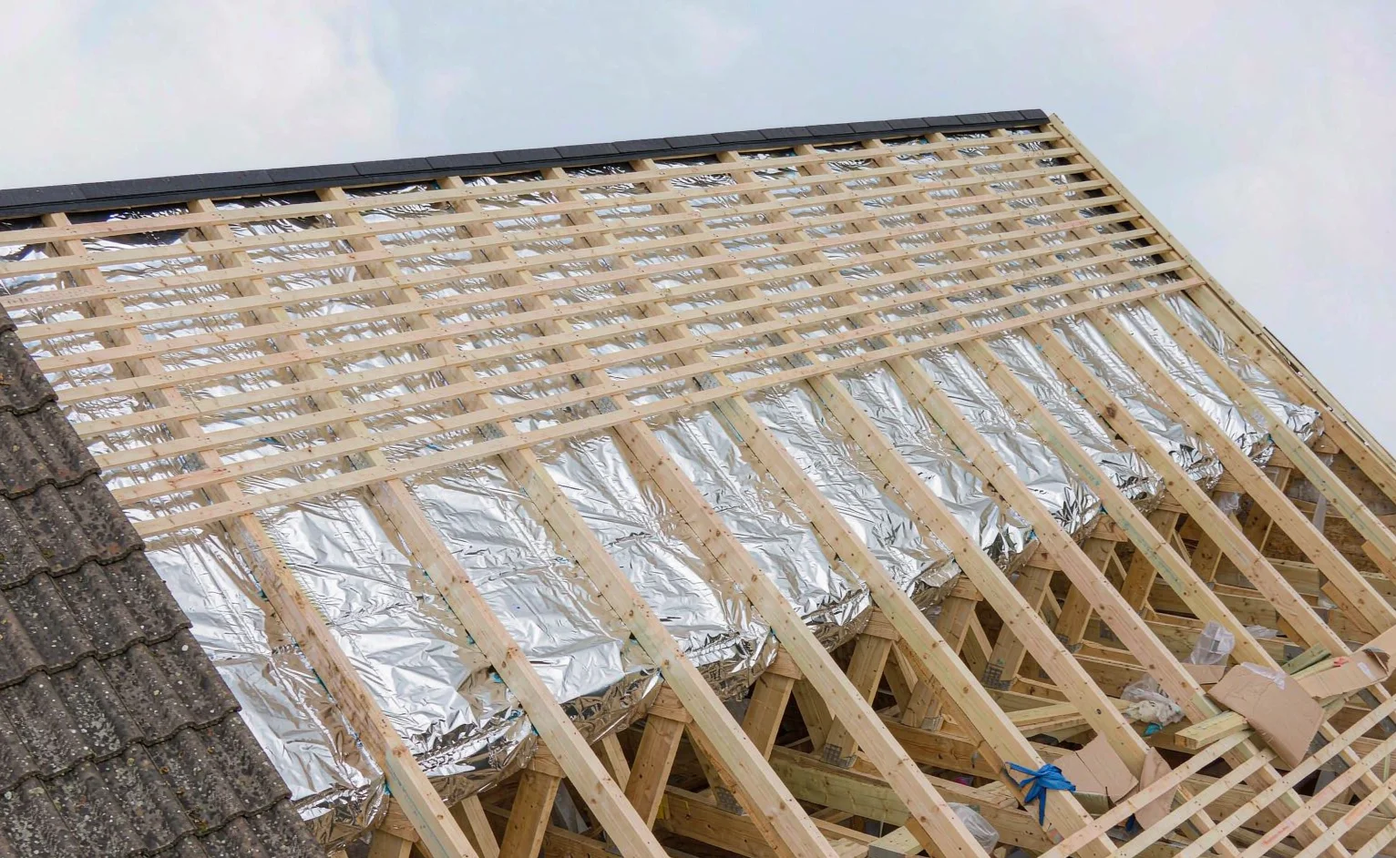 Pitched roof build-up under construction showing timber battens over a reflective foil layer with ridge ventilation at the apex
