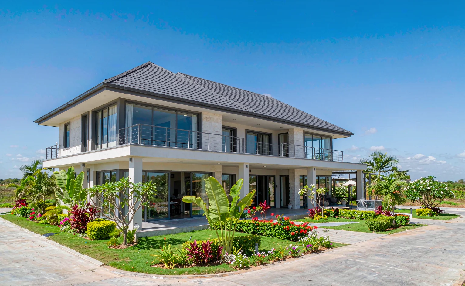 Two-storey East African villa with a charcoal stone-coated metal tile roof under strong equatorial sunlight