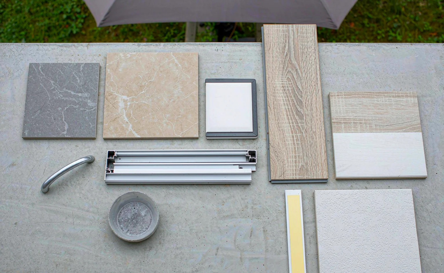 Flat lay of a whole-house material sample board with porcelain tiles, SPC flooring planks, aluminium window profile, cabinet door sample and paint swatch