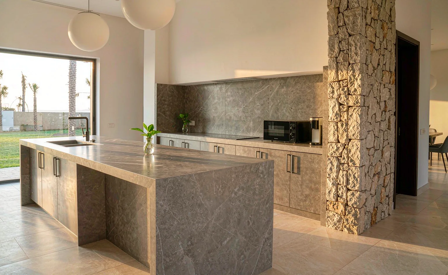 Open-plan villa kitchen with a jointless 12 mm sintered stone island worktop and full-height slab backsplash in warm grey