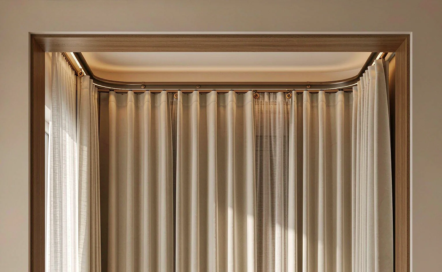 Curtain track with rings and heavy cream drape in a ceiling recess with warm LED strip behind, sheer white voile layer in front