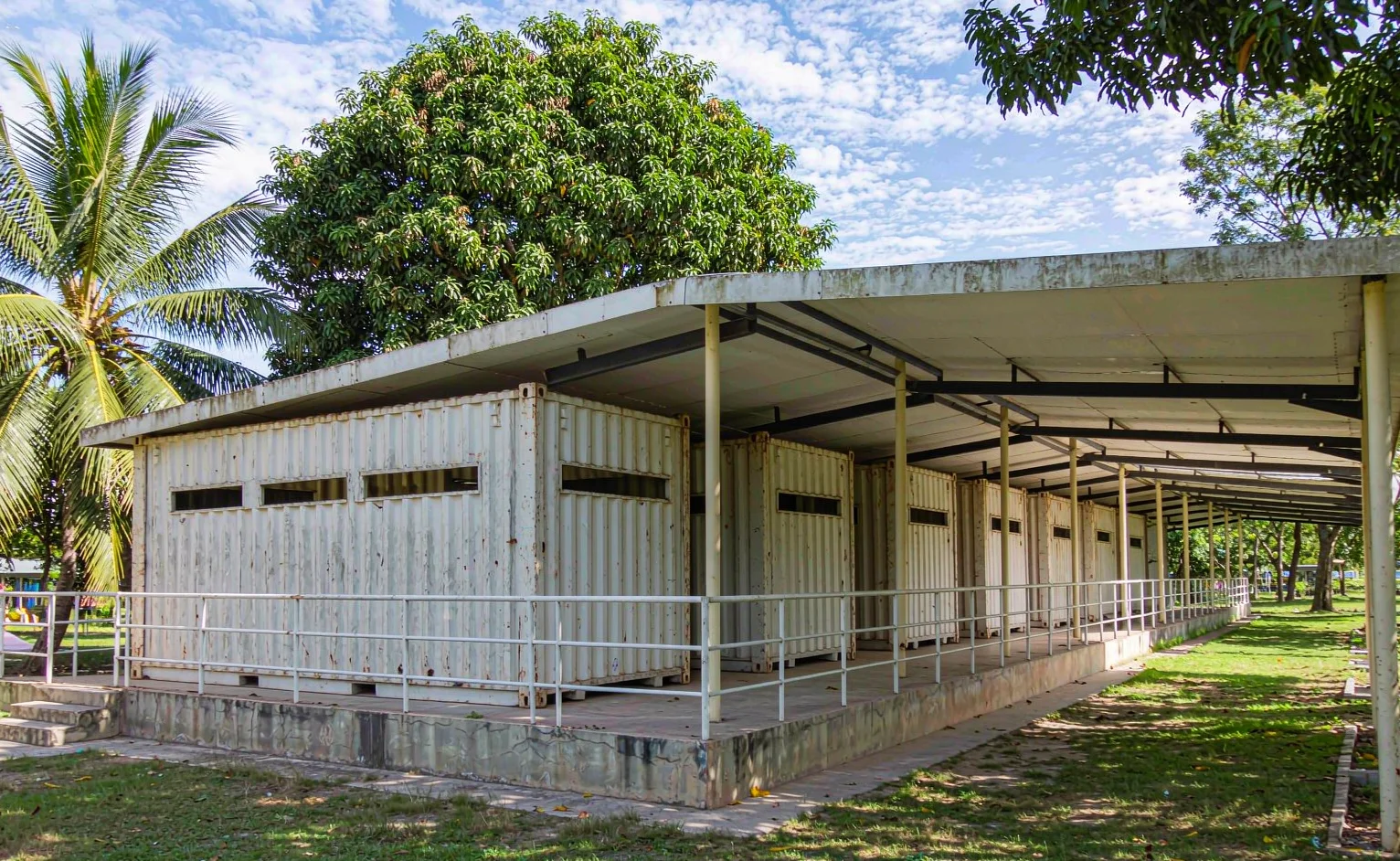 Row of shipping containers converted into school classrooms with a shaded veranda corridor in a tropical schoolyard