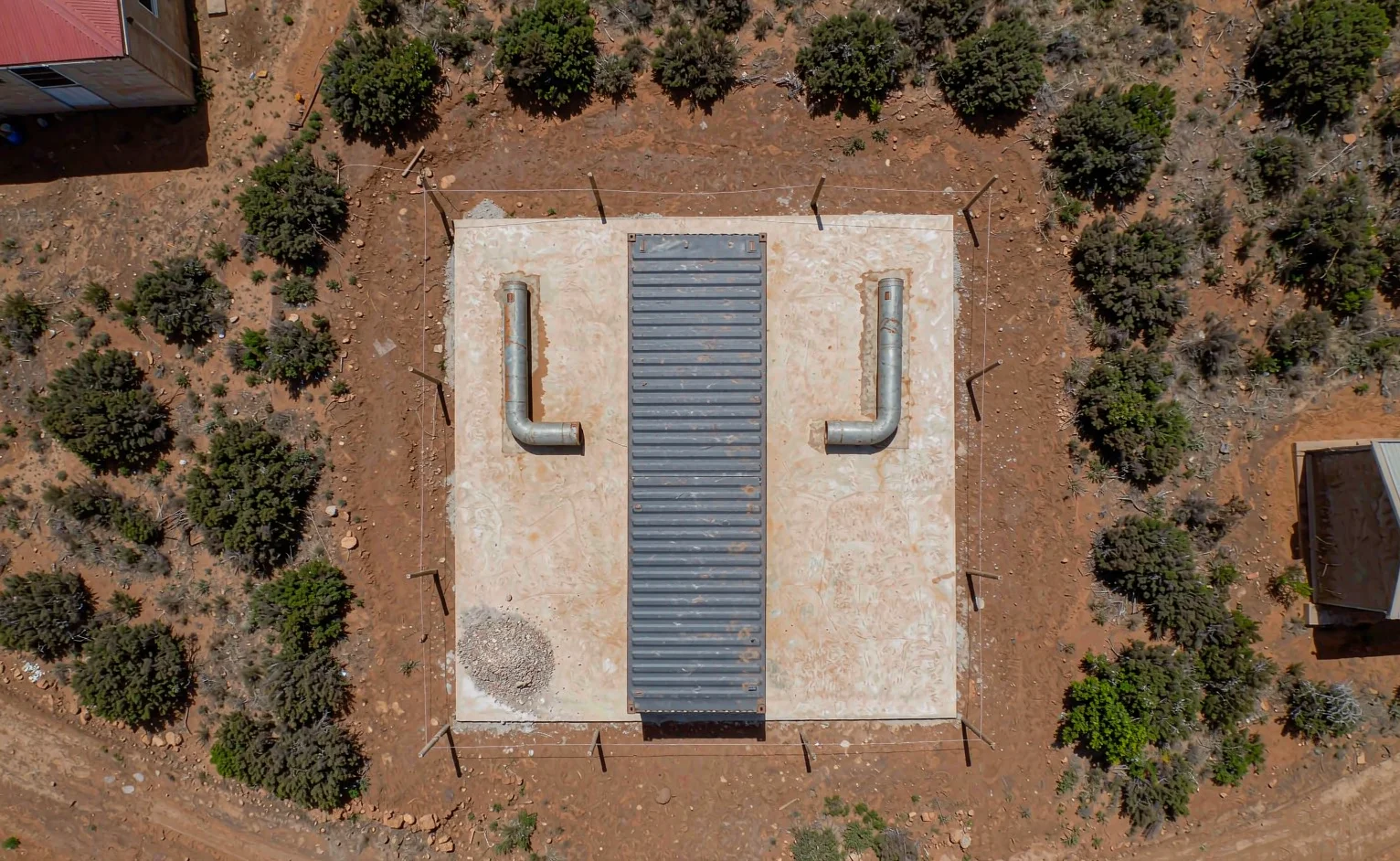 Aerial view of a 40 foot shipping container set on levelled concrete pad foundations with screw pile anchors on a red earth site