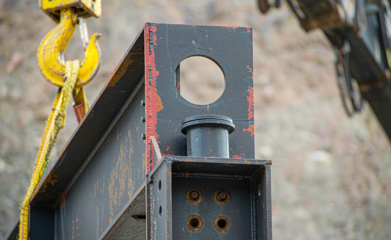 Close-up of a painted structural steel connection with bolts and a yellow crane hook lifting a beam on an African construction site