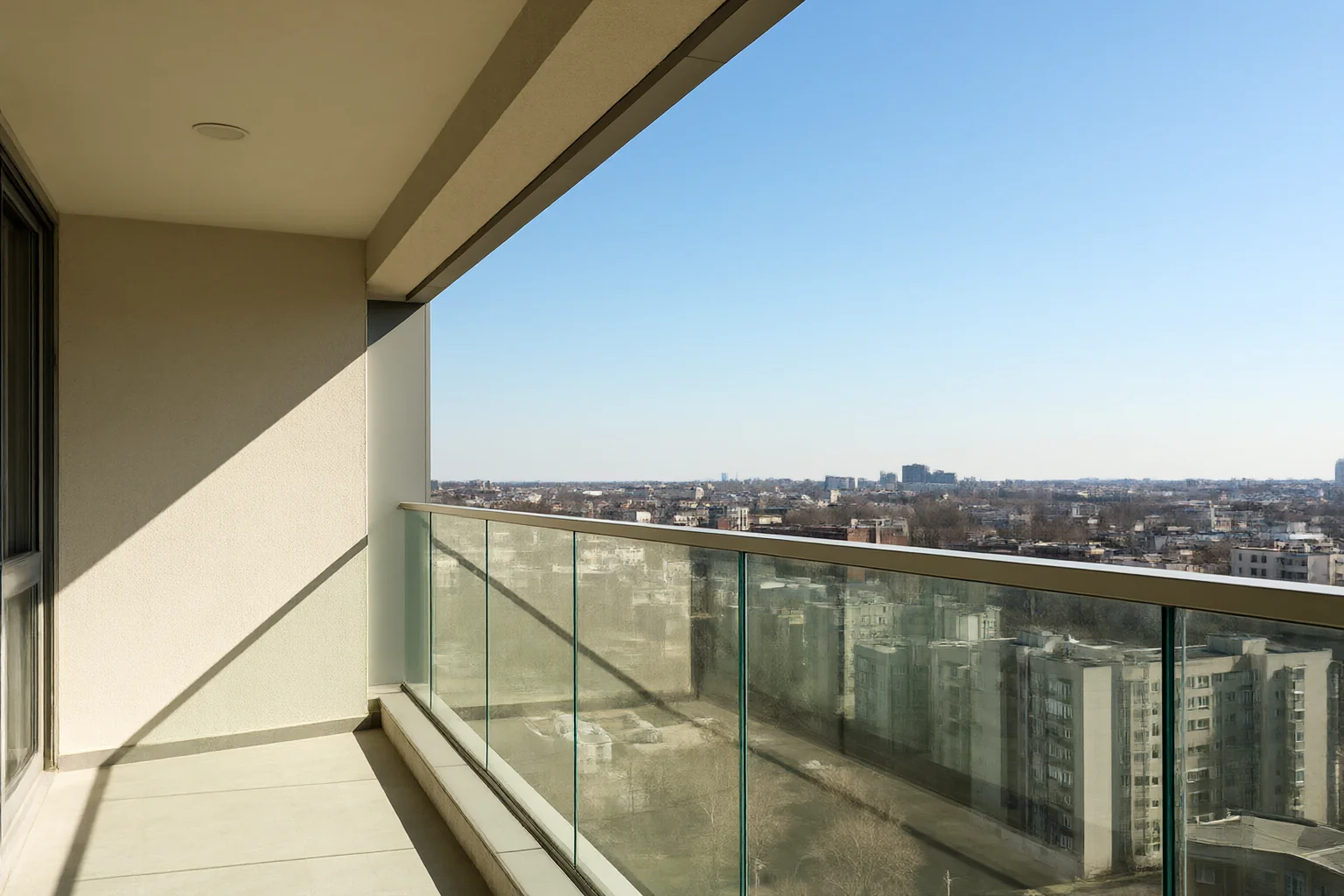 Glass balcony railing on a sunny apartment terrace with a city skyline behind