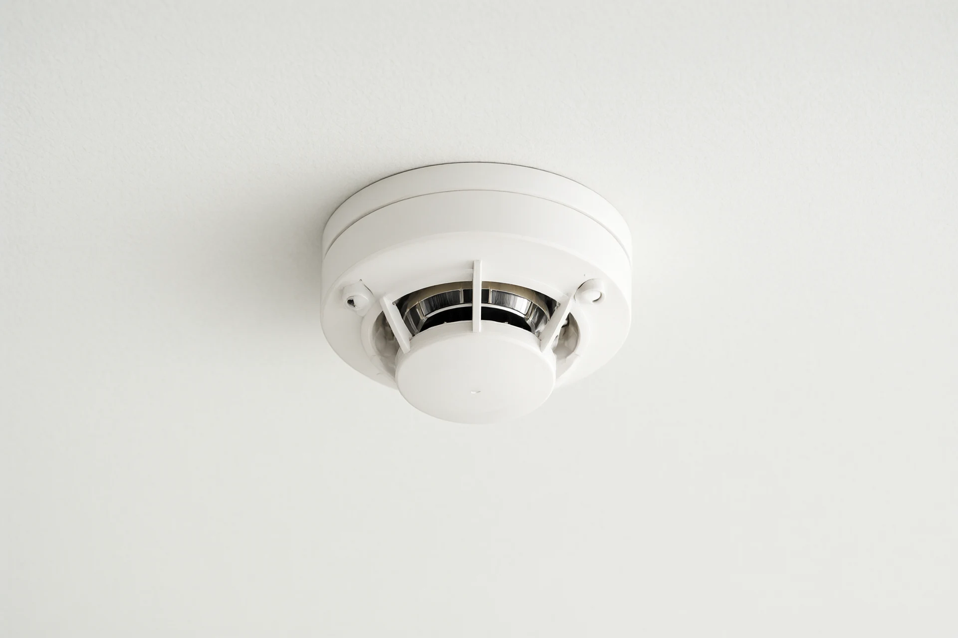 White ceiling-mounted photoelectric smoke detector, minimalist industrial design, studio product shot